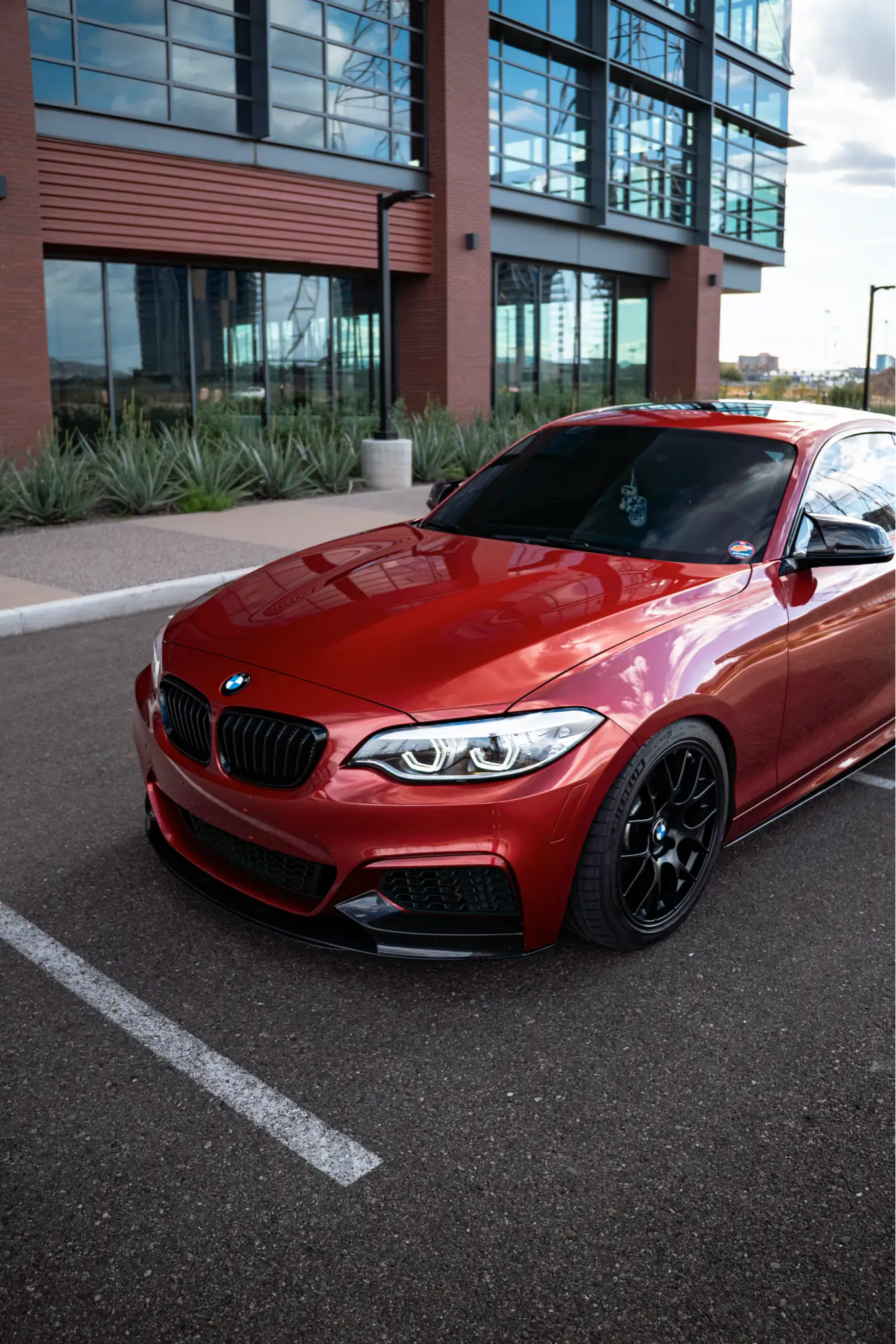Red BMW 240i shown front three-quarter in an office plaza parking area.