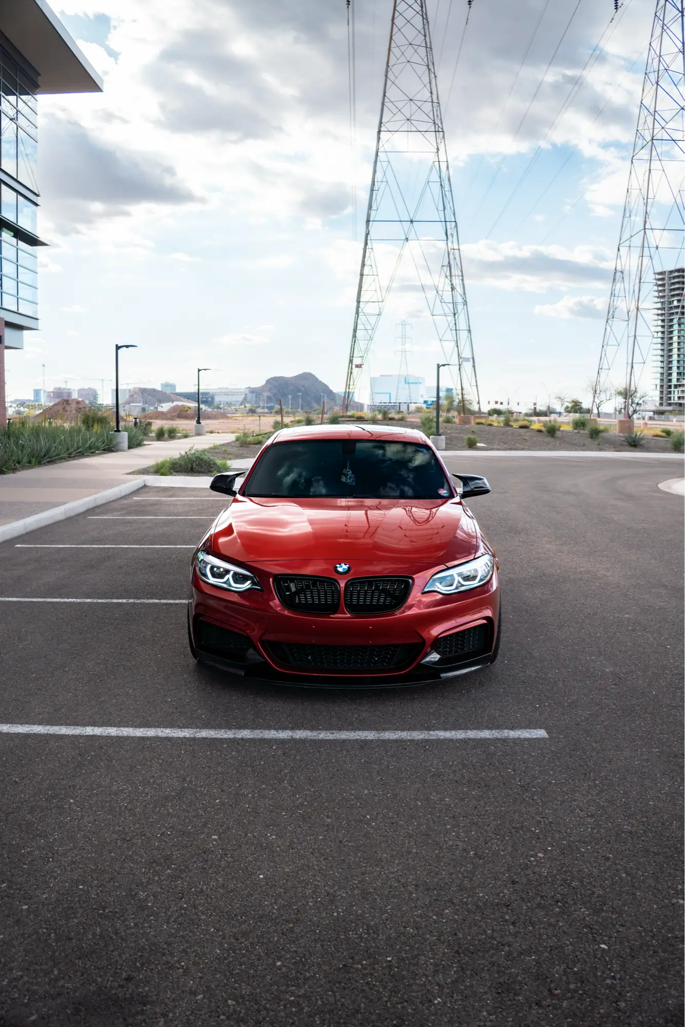 Straight-on front view of a red BMW 240i with transmission towers in the background.