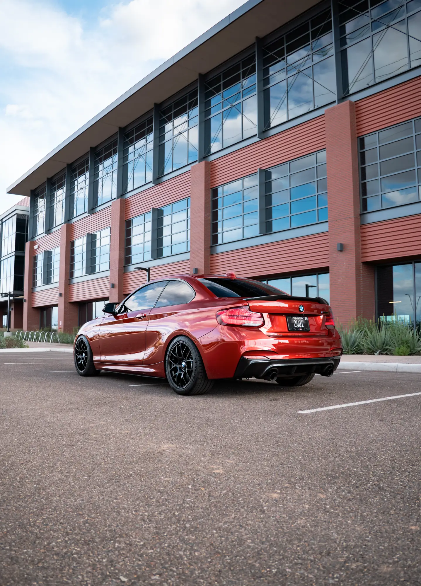 Red BMW 240i shown rear three-quarter in front of an office building.