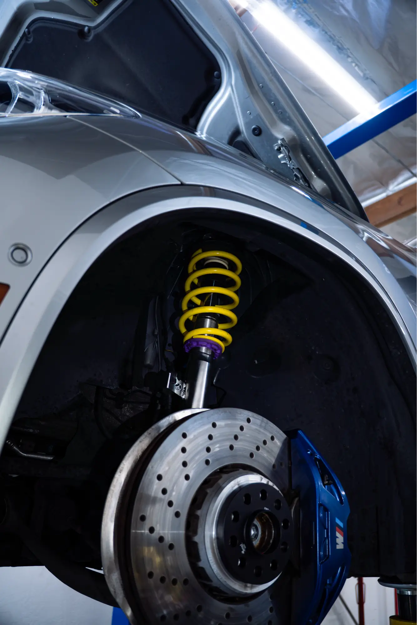 Close-up of a yellow coilover suspension spring installed in a car's wheel well, a performance upgrade at HTP Motorsport.