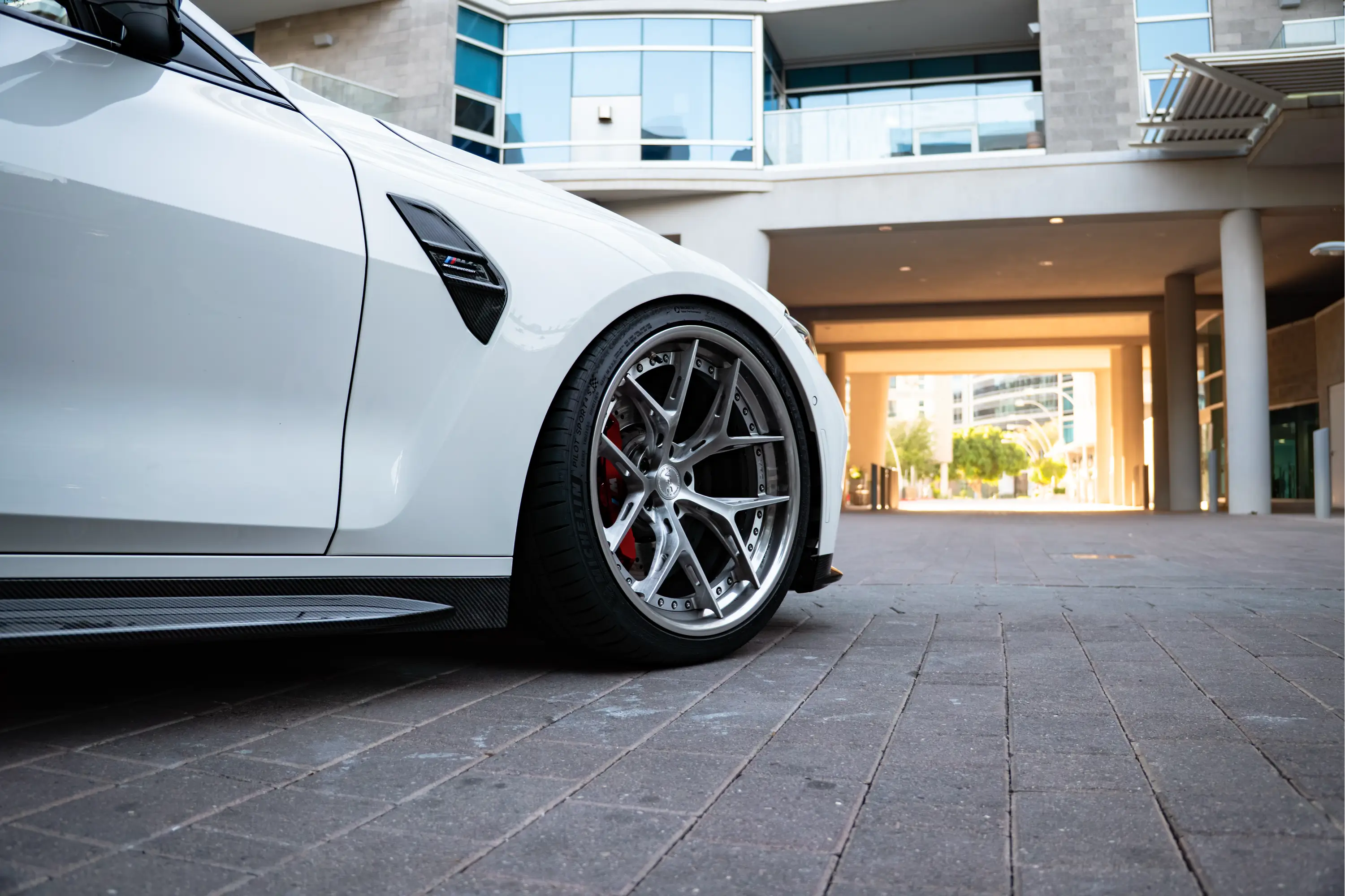 Close-up of a white BMW M4 Competition's front wheel, representative of HTP Motorsport's wheel and tire services.