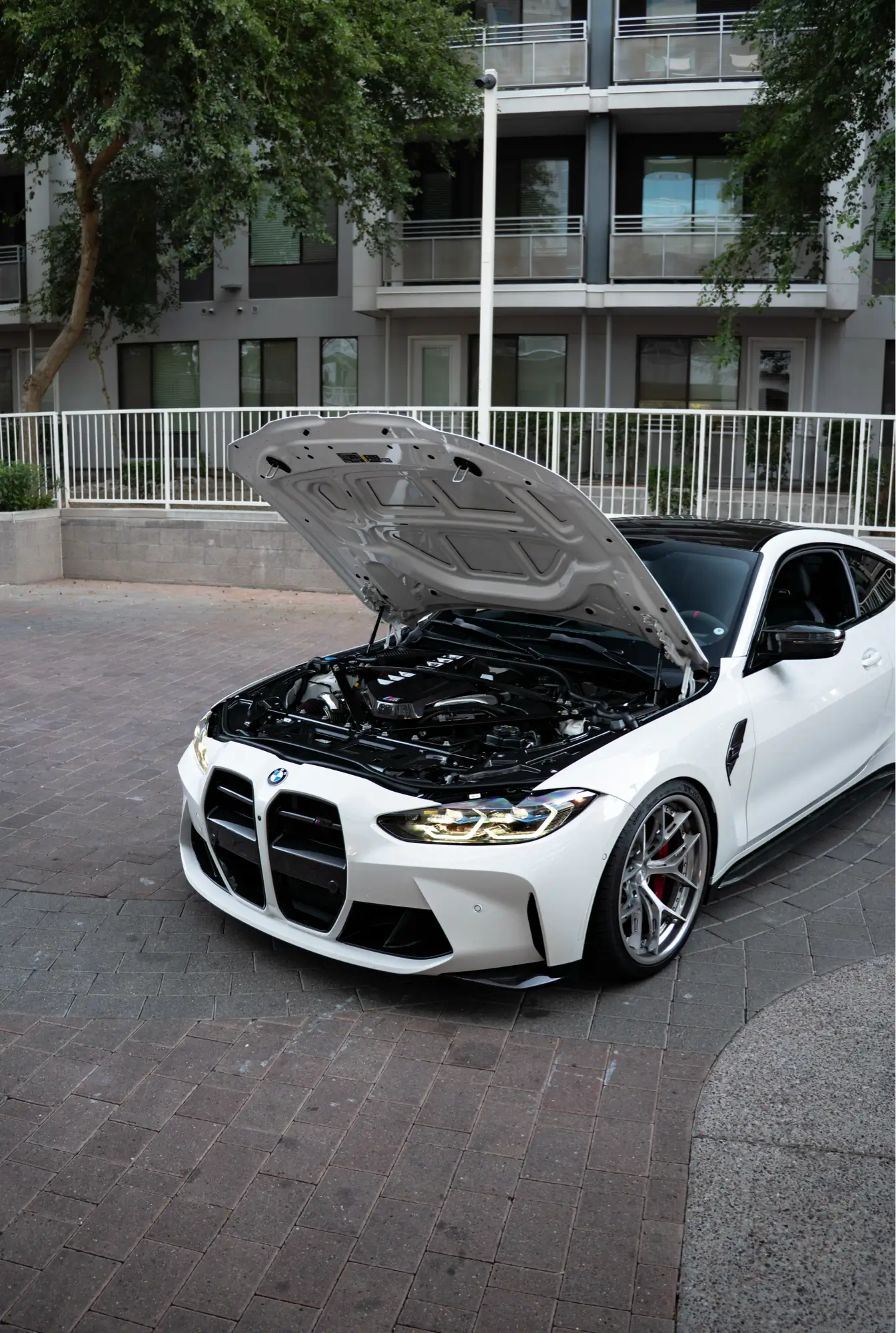 White BMW M4 (G82) with its hood open, front three-quarter view, prepped for performance tuning work.