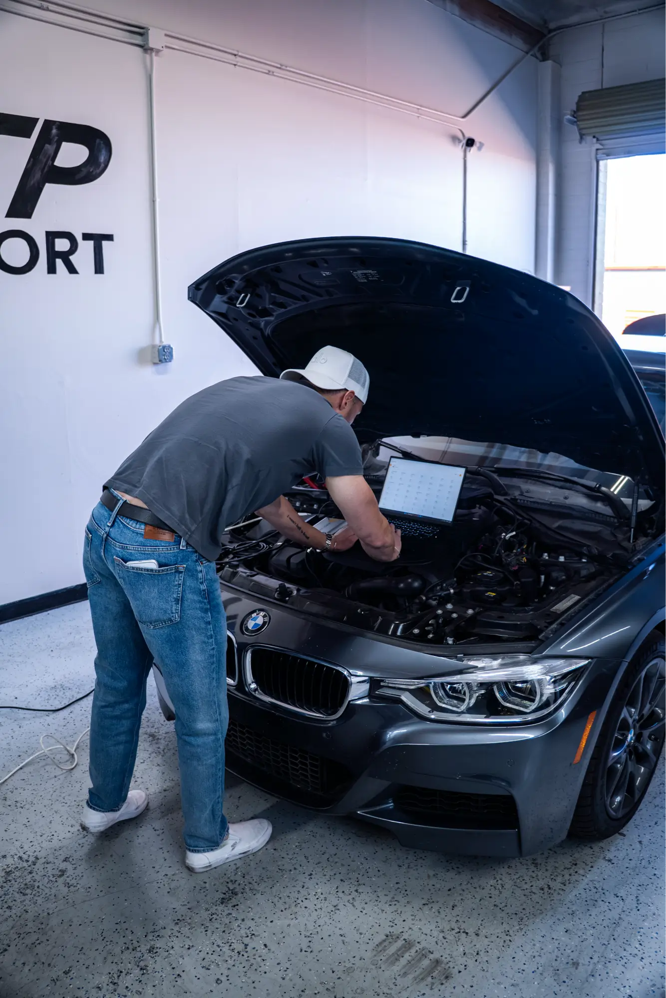 HTP Motorsport technician running a diagnostic scan with a laptop on a BMW F30's engine bay.
